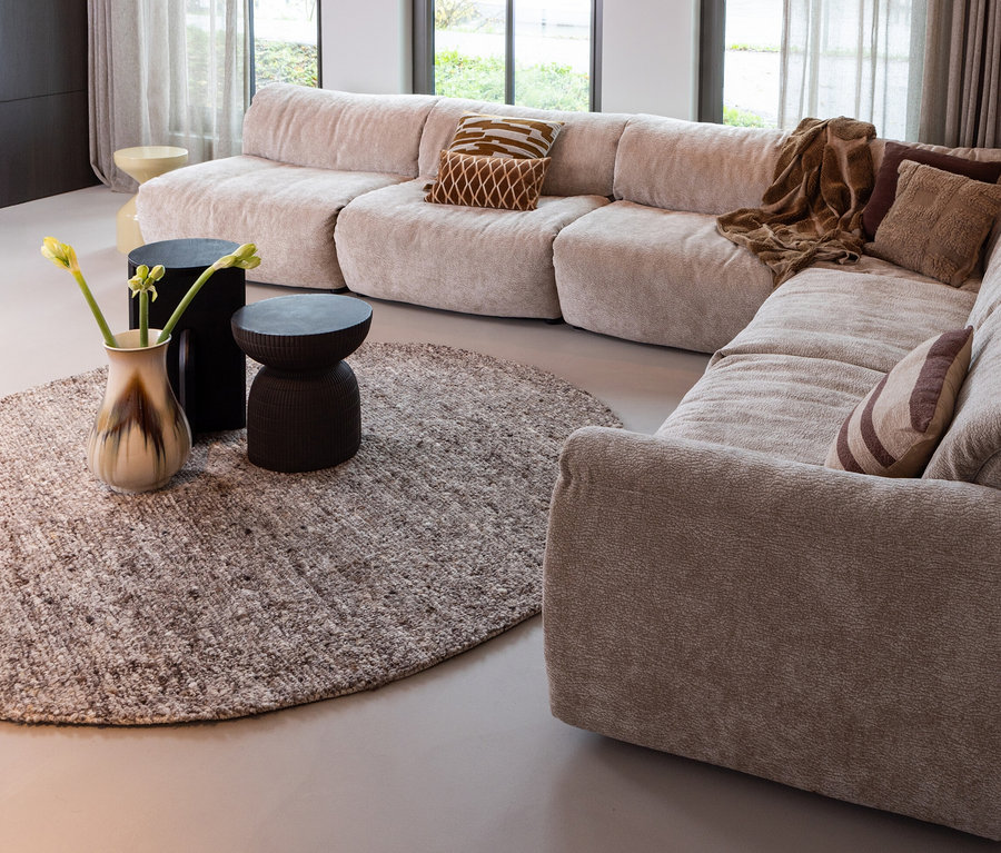 Beiges modulares Sofa mit braunen Kissen und Überwurf auf dem runden Teppich »Efia« von Woood.