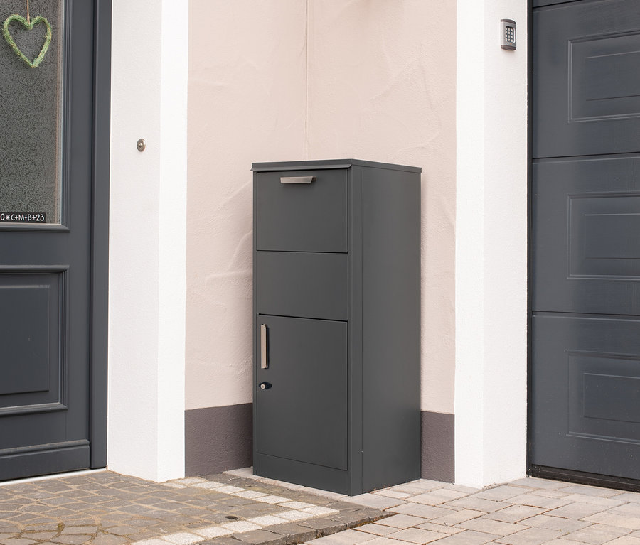 Eine graue Paketbox steht vor einer Haustür.