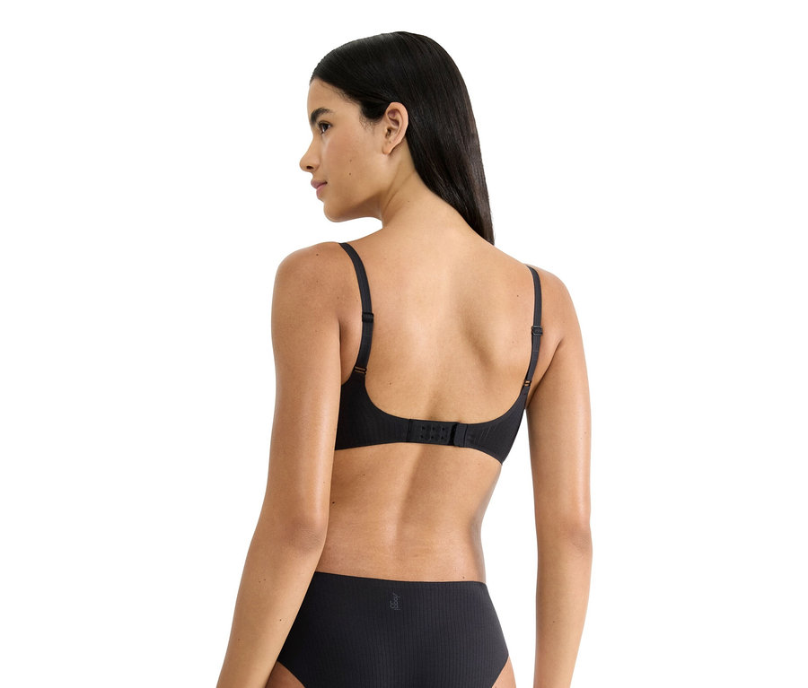 Rückansicht einer Frau mit langen, dunklen Haaren, die einen schwarzen BH und Unterwäsche trägt.