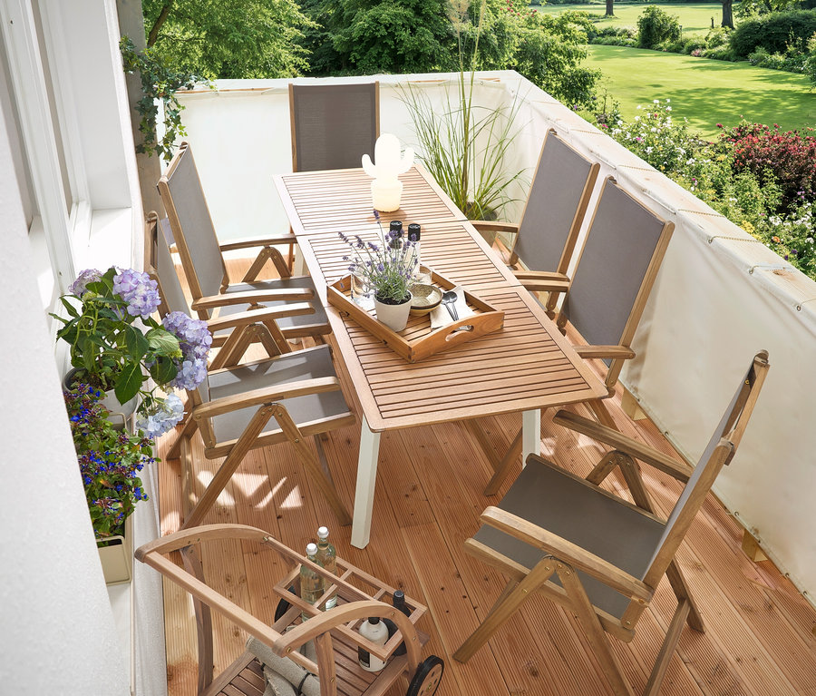 Auf einem Balkon stehen ein schmaler, ausziehbarer Gartentisch »Liska«, ein creme Balkon Sicht- und Windschutz, ein Barwagen mit abnehmbarem Tablett und eine LED-Outdoor-Akku-Tischleuchte in Kaktusform.