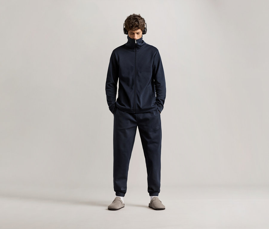 Mann mit Kopfhörern, der einen dunkelblauen Hausanzug trägt.