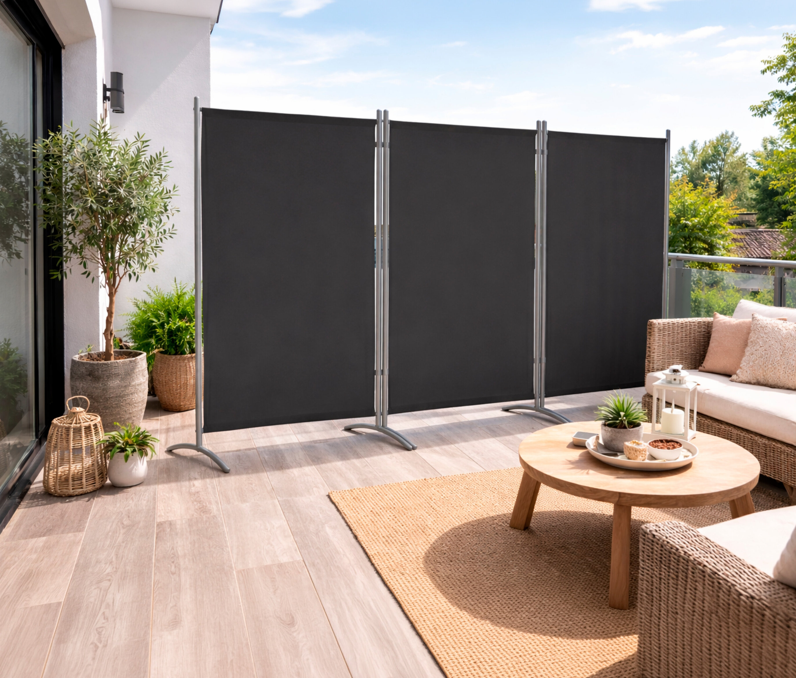 Auf einer Terrasse steht eine anthrazitfarbene, 3-teilige Leco Stellwand. Davor sind ein Tisch, ein Sofa und Pflanzen zu sehen.