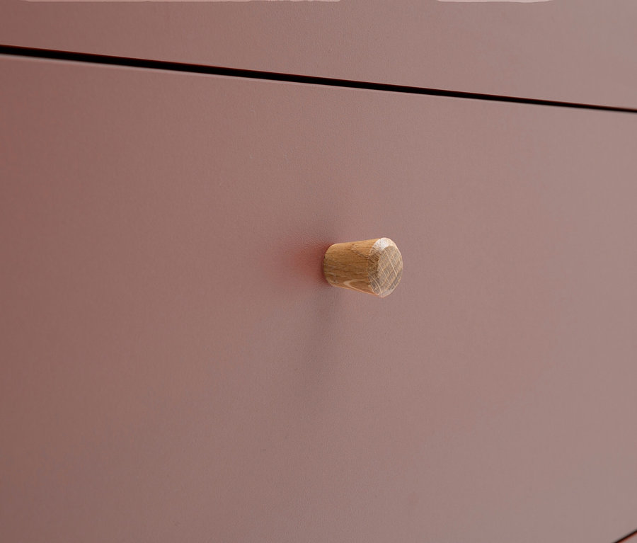 Nahaufnahme einer rosafarbenen Kommode mit einem runden Holzgriff.