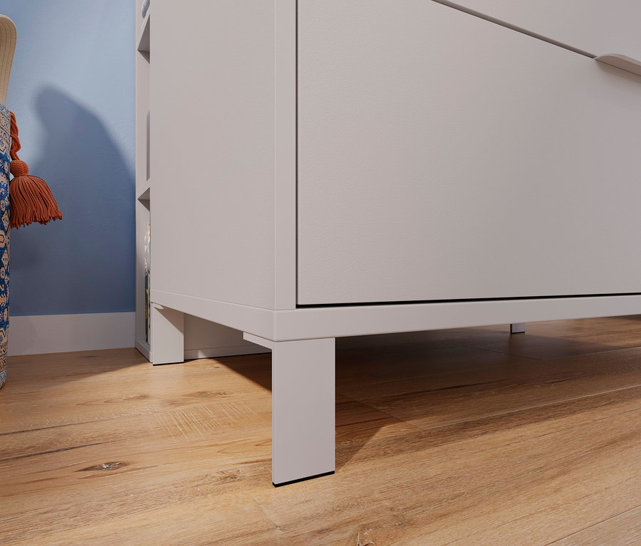 Detailansicht eines hellgrauen Schubladenschranks auf einem Holzboden, daneben eine blaue Stofftasche mit orangefarbenen Quasten.