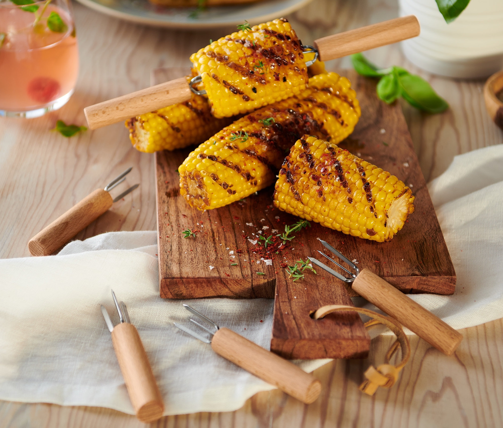 Gegrillter Mais auf einem Holzbrett mit 8 Maiskolbenhaltern.
