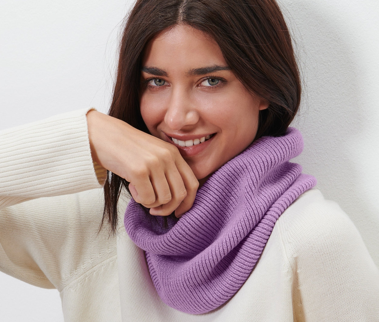 Frau mit braunen Haaren lächelt und trägt einen Strick-Loop.