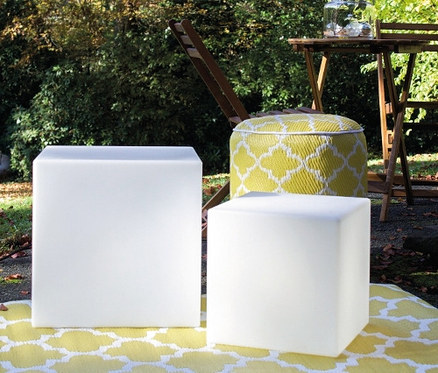 Zwei weiße 8 seasons design LED-Leuchtwürfel und ein gelber Hocker auf einem gelben Teppich im Freien.