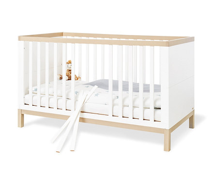 Pinolino Babybett »Light« mit weißen Gitterstäben und Holzrahmen. Im Inneren liegen eine Plüschgiraffe und eine weiße Decke mit blauen Sternen.