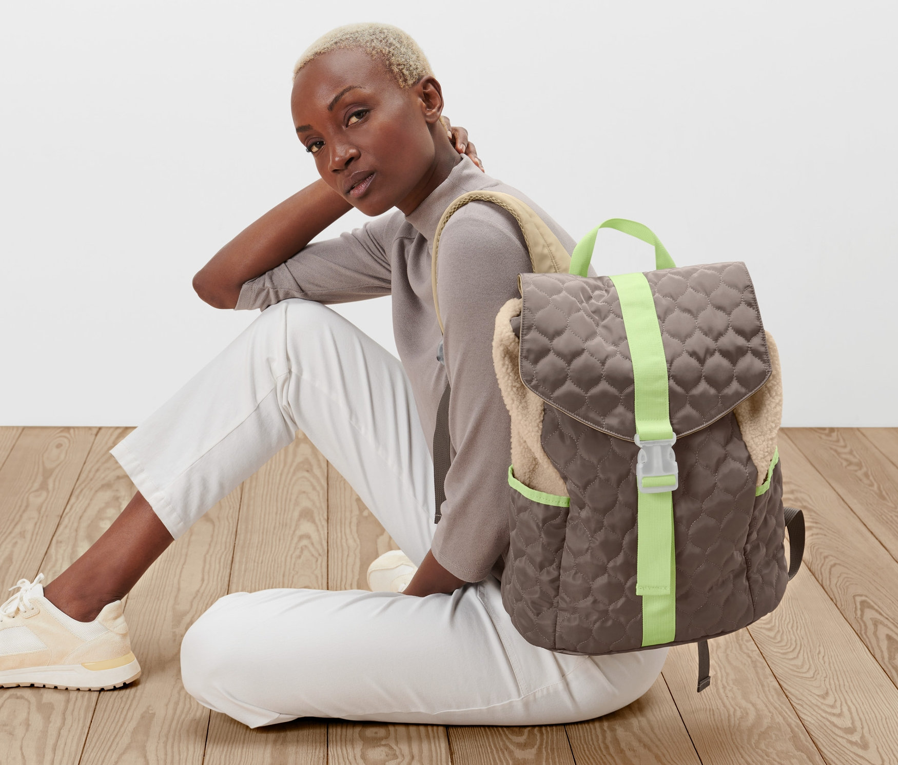 Frau sitzt auf dem Boden neben Rucksack in Steppoptik.