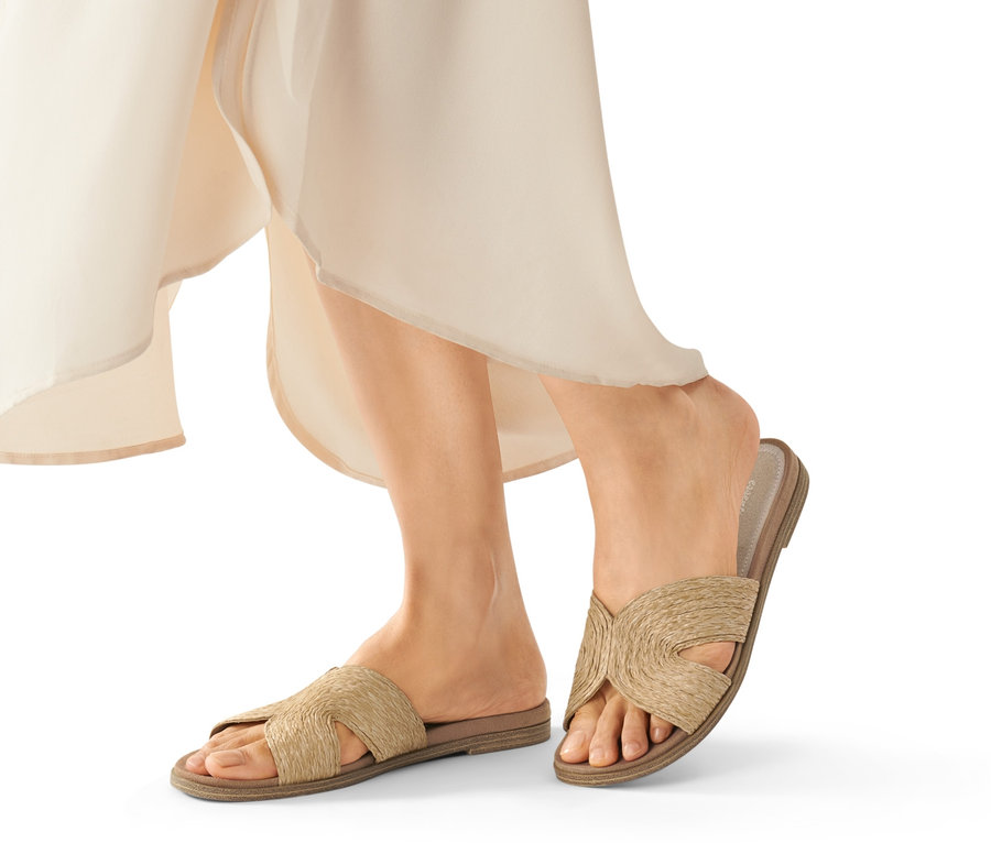 Beine einer Frau, die beige Pantoletten trägt.