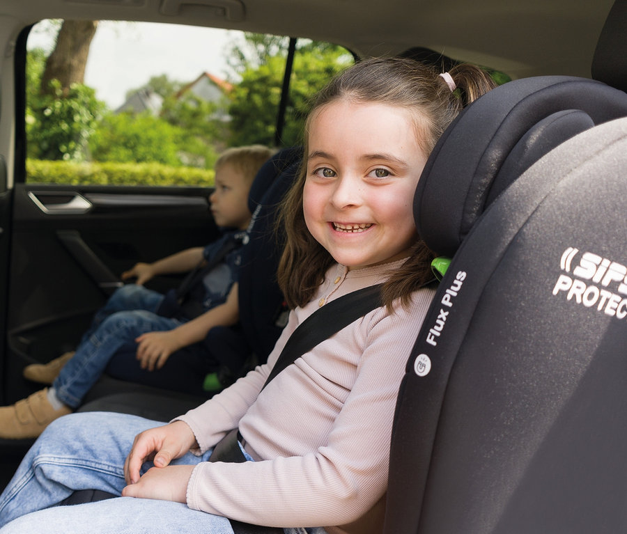 Lächelndes Mädchen sitzt im Osann Kindersitz »Flux Plus«, im Hintergrund sitzt ein Junge.