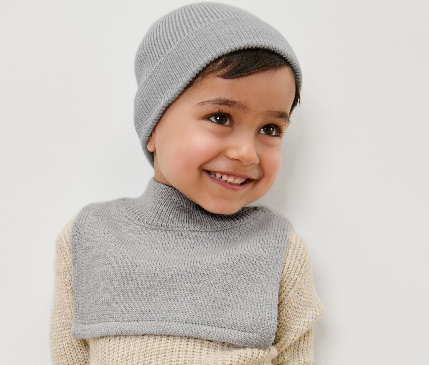 Ein lächelnder Junge trägt einen Kinder-Woll-Rollkragenschal und eine Mütze.