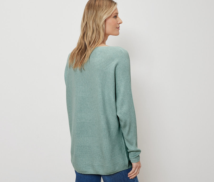 Frau posiert in Feinstrickpullover, salbei, und blauen Jeans.