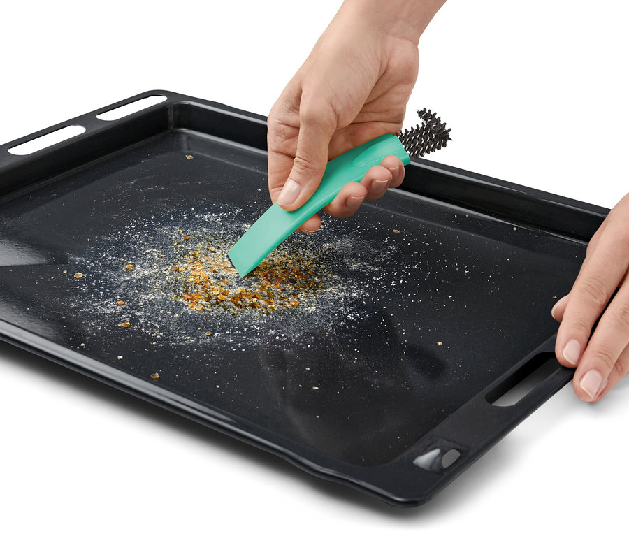 Eine Hand reinigt ein schwarzes Backblech mit einer Backofenbürste mit Schaber.