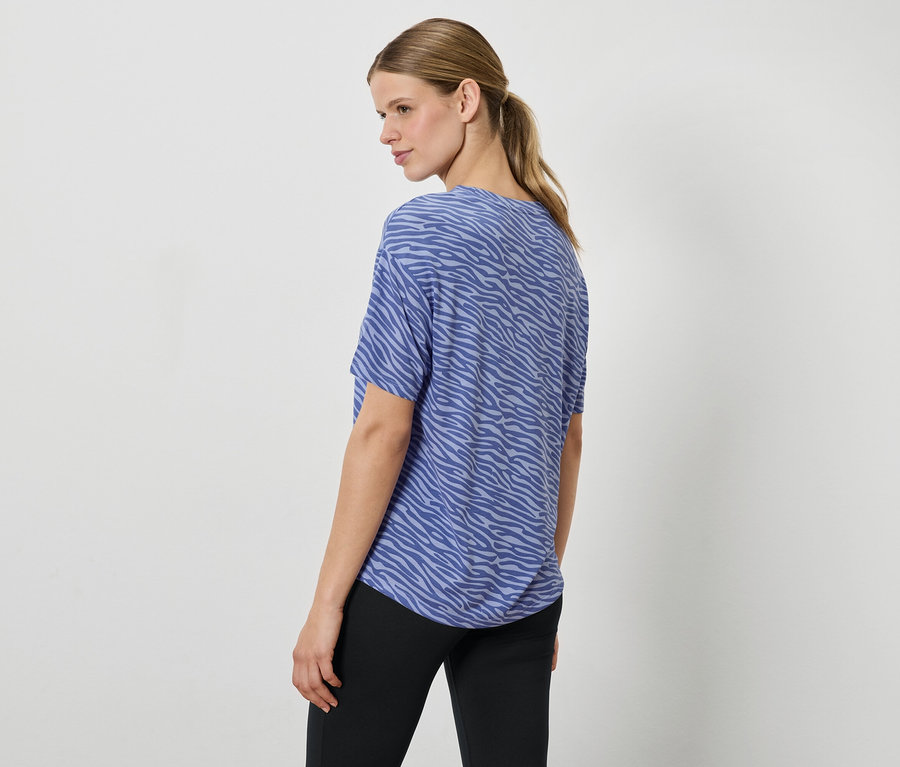 Eine Frau mit einem blauen Animal-Print-Top und schwarzen Hosen, die über die Schulter schaut.