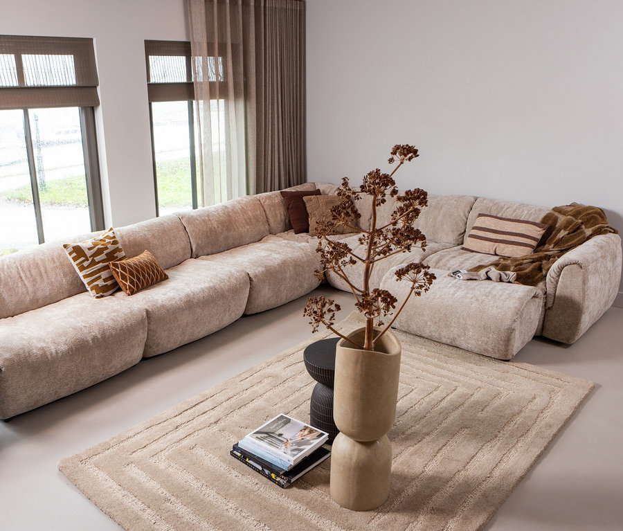 Beiges Ecksofa mit Kissen und brauner Decke steht auf dem beigen Woood Teppich Alicia.