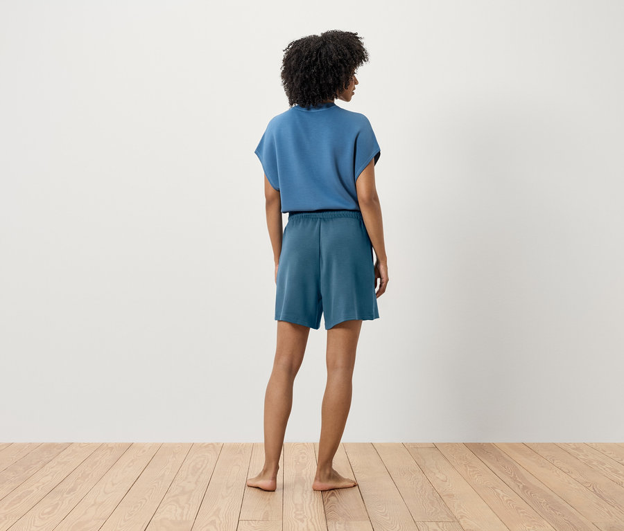 Frau in blauem T-Shirt und Shorts steht mit dem Rücken zur Kamera.