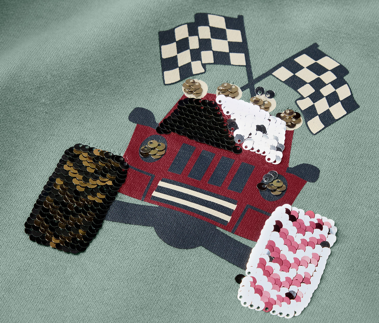 Detail eines Kinder-Sweatshirts mit Truck-Applikation und karierten Flaggen.