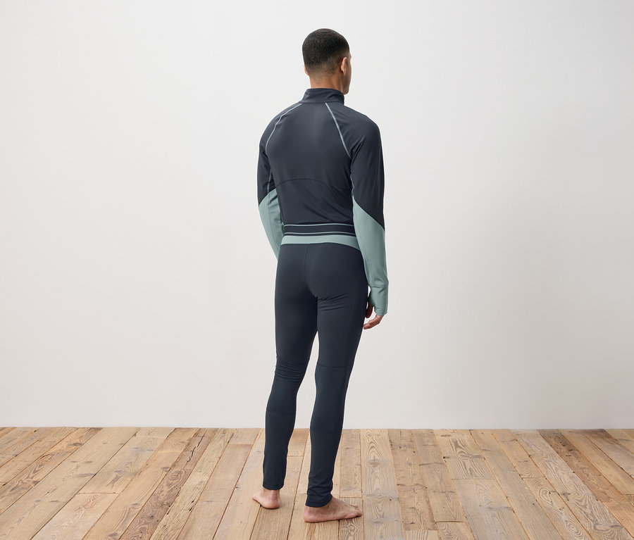 Mann von hinten in dunkelgrauer Thermobekleidung auf Holzboden.