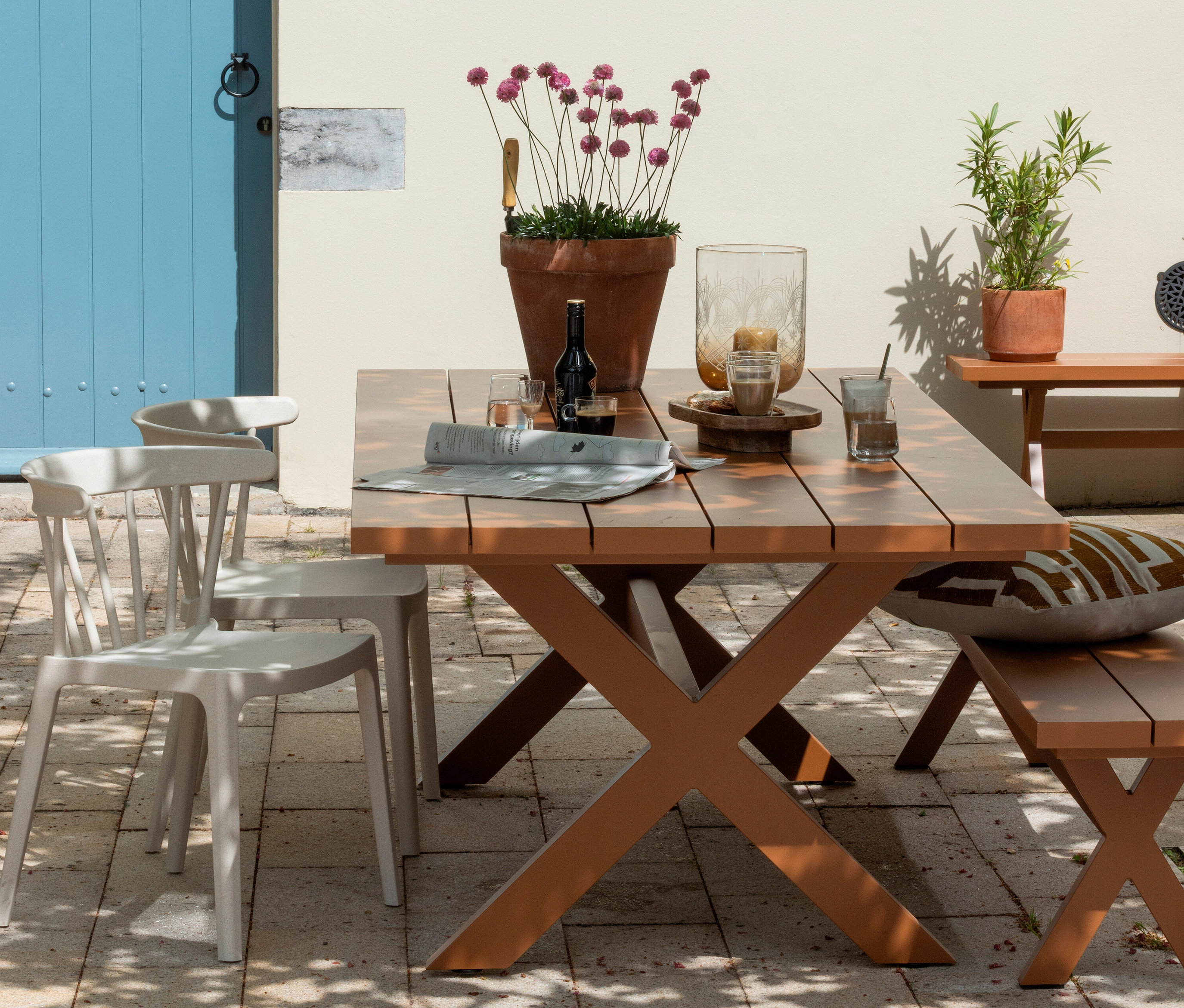 Esstisch mit Getränken, Zeitung und Blumentopf im Freien.