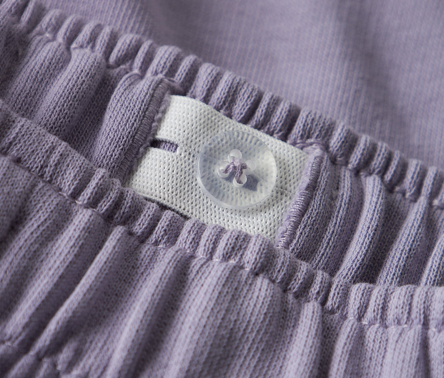 Nahaufnahme vom Bund einer lila Hose mit verstellbarem Gummizug und Knopf.