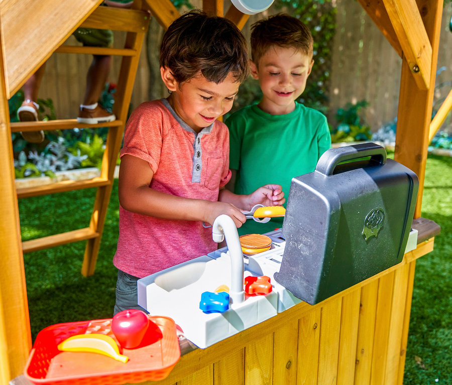 Zwei Kinder spielen im Spielturm »Bolzo« mit Spielzeugküche und Grill.