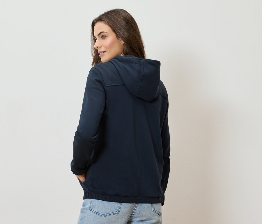 Eine Frau trägt einen marineblauen Kapuzenpullover und hellblaue Jeans.