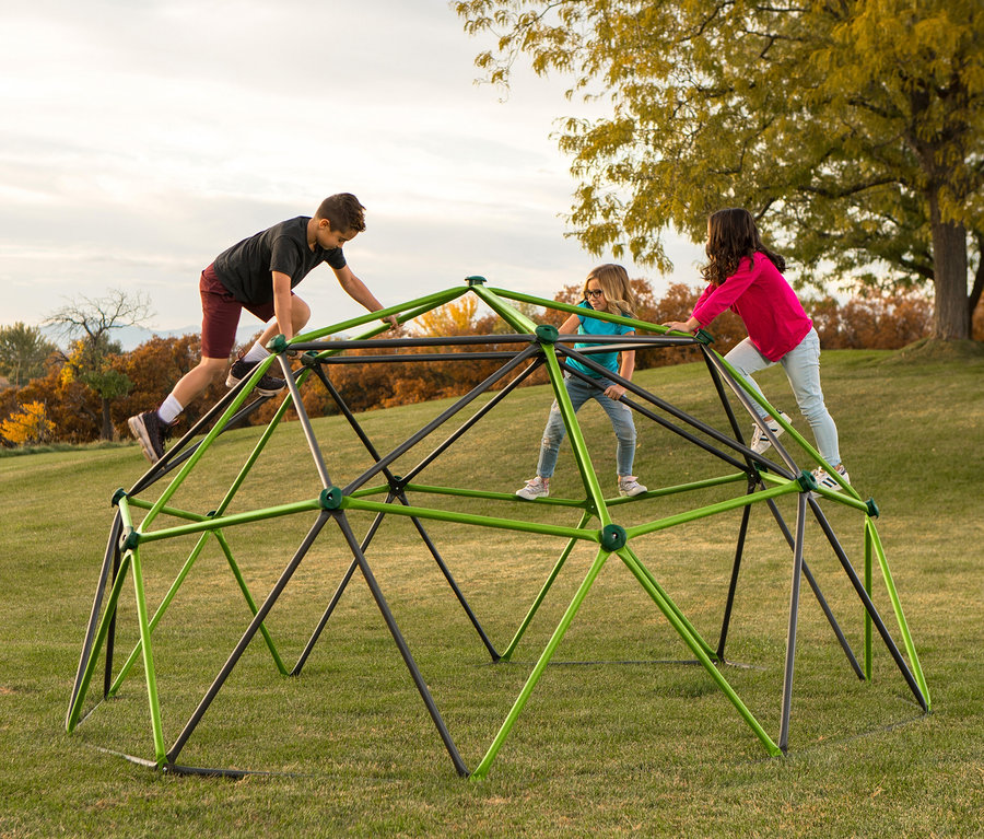 Drei Kinder klettern auf ein großes LIFETIME-Klettergerüst »Geodome« auf einer Wiese.
