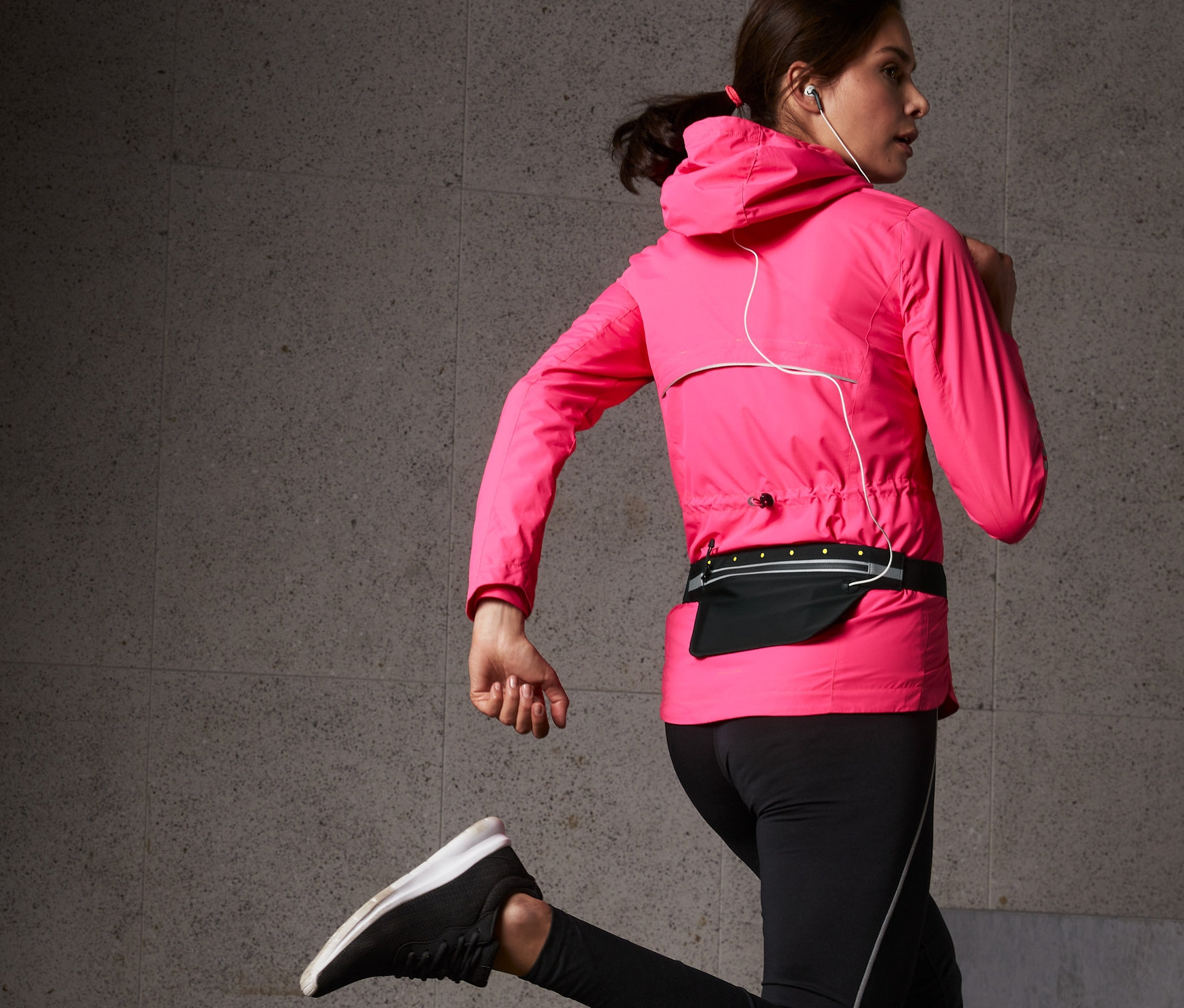 Frau in pinker Jacke und schwarzen Leggings joggt mit einem schwarzen LED-Laufgürtel für Smartphones.