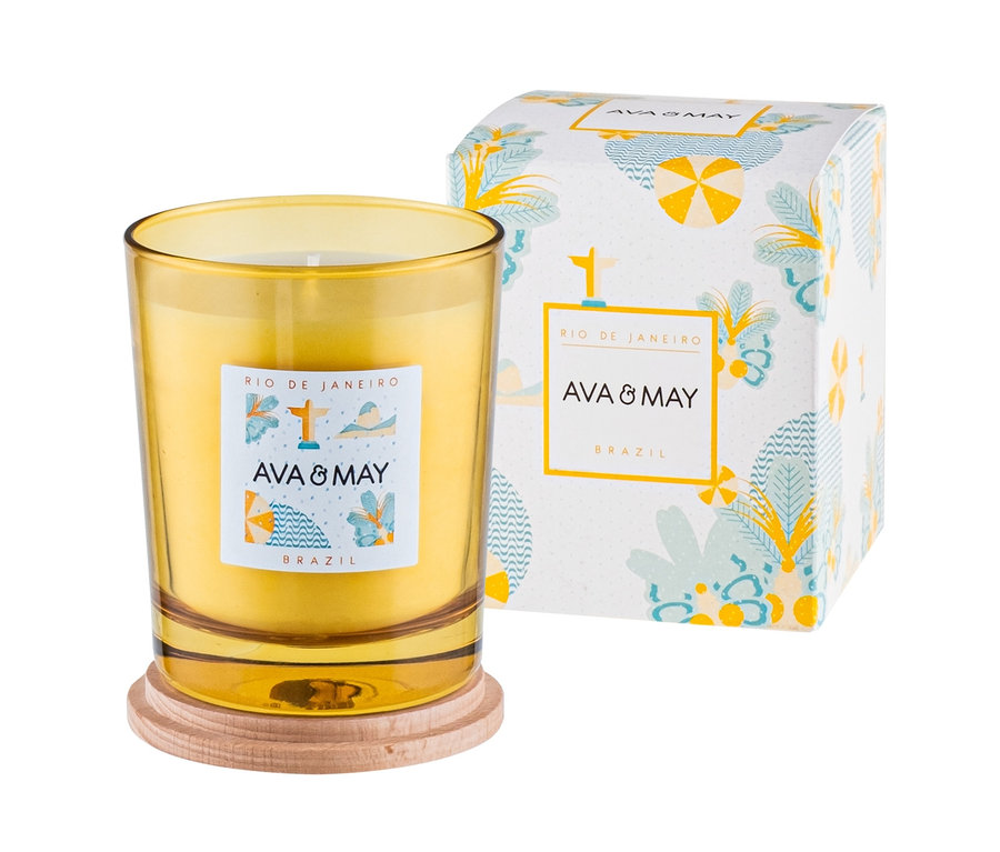 Gelbe Duftkerze „Rio de Janeiro“ von Ava & May auf Holzuntersetzer neben Verpackung.