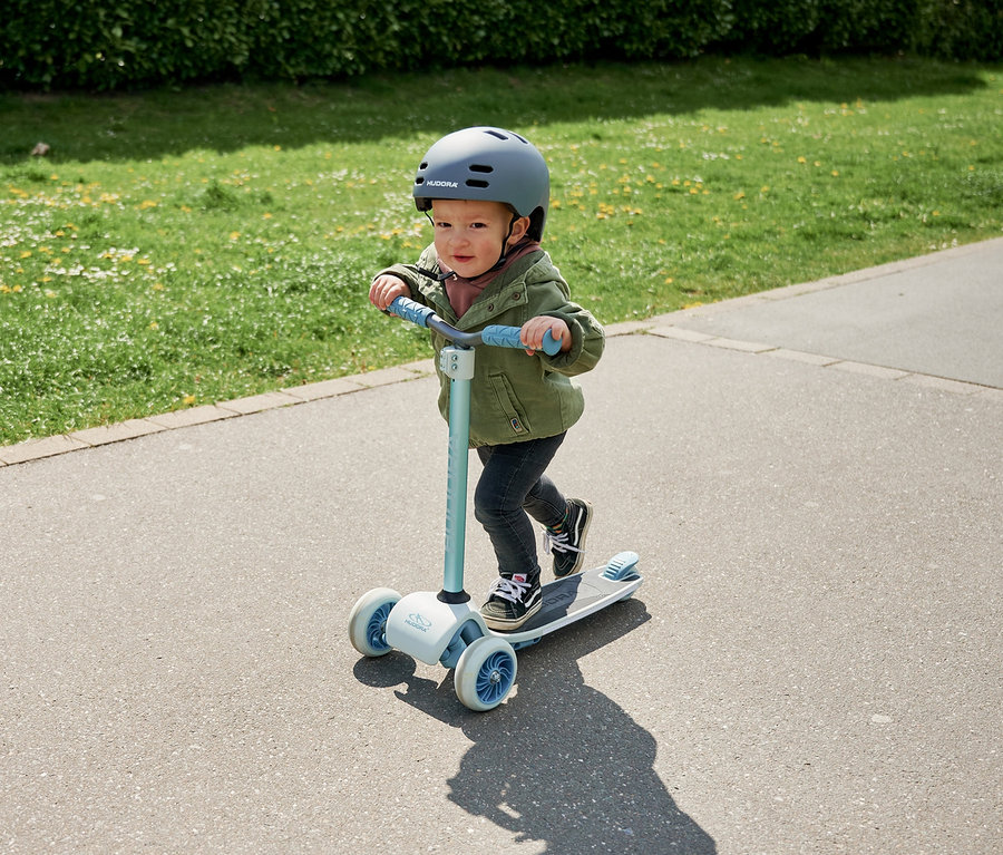 Kind mit Helm fährt mit blauem HUDORA Tri-Scooter auf dem Gehweg.
