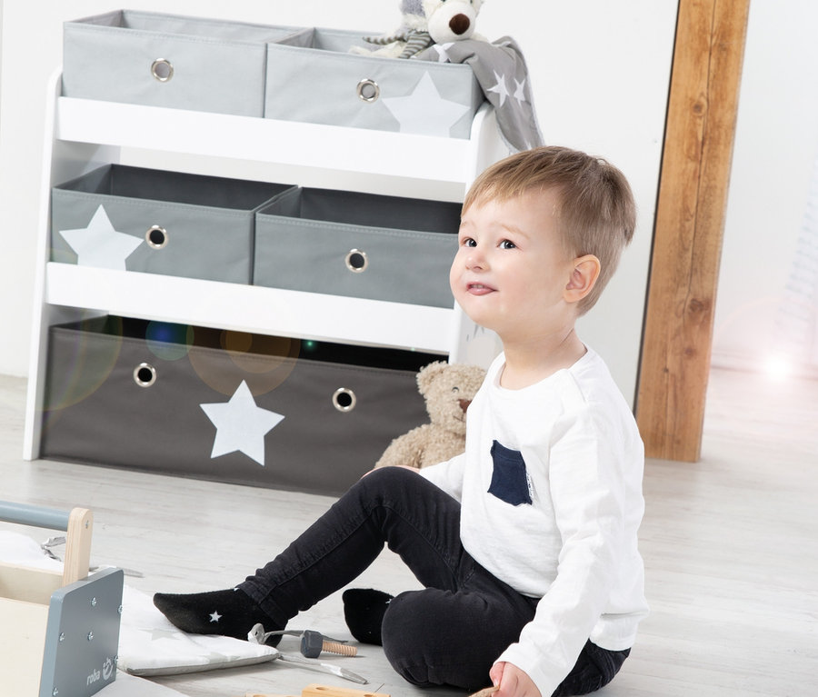 Ein Junge sitzt auf dem Boden und spielt mit Spielzeug. Im Hintergrund ist ein roba Spielregal "Stars" zu sehen.