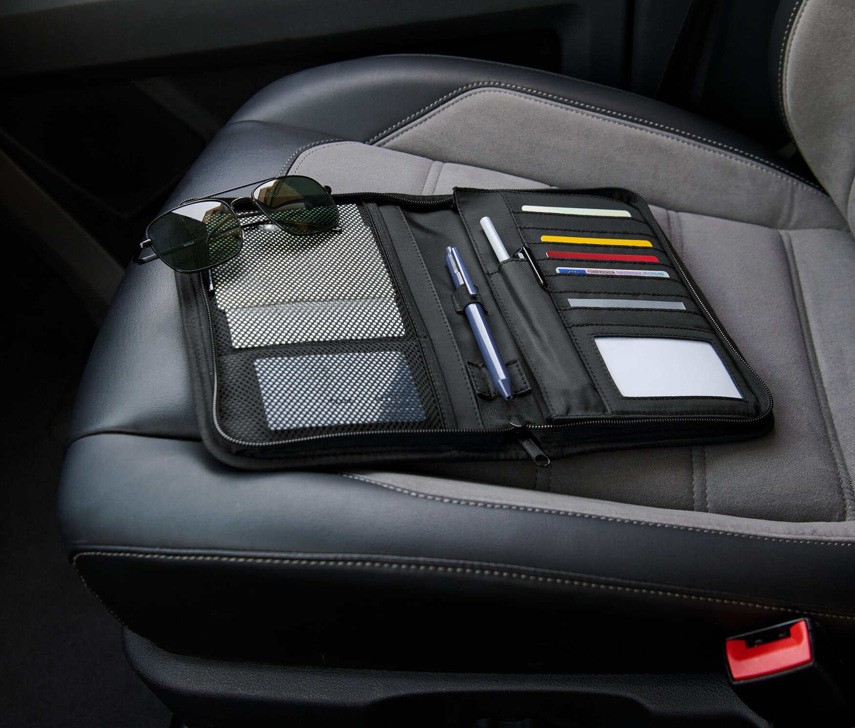 Ein schwarzer Handschuhfach-Organizer liegt offen auf einem Autositz neben einer Sonnenbrille.