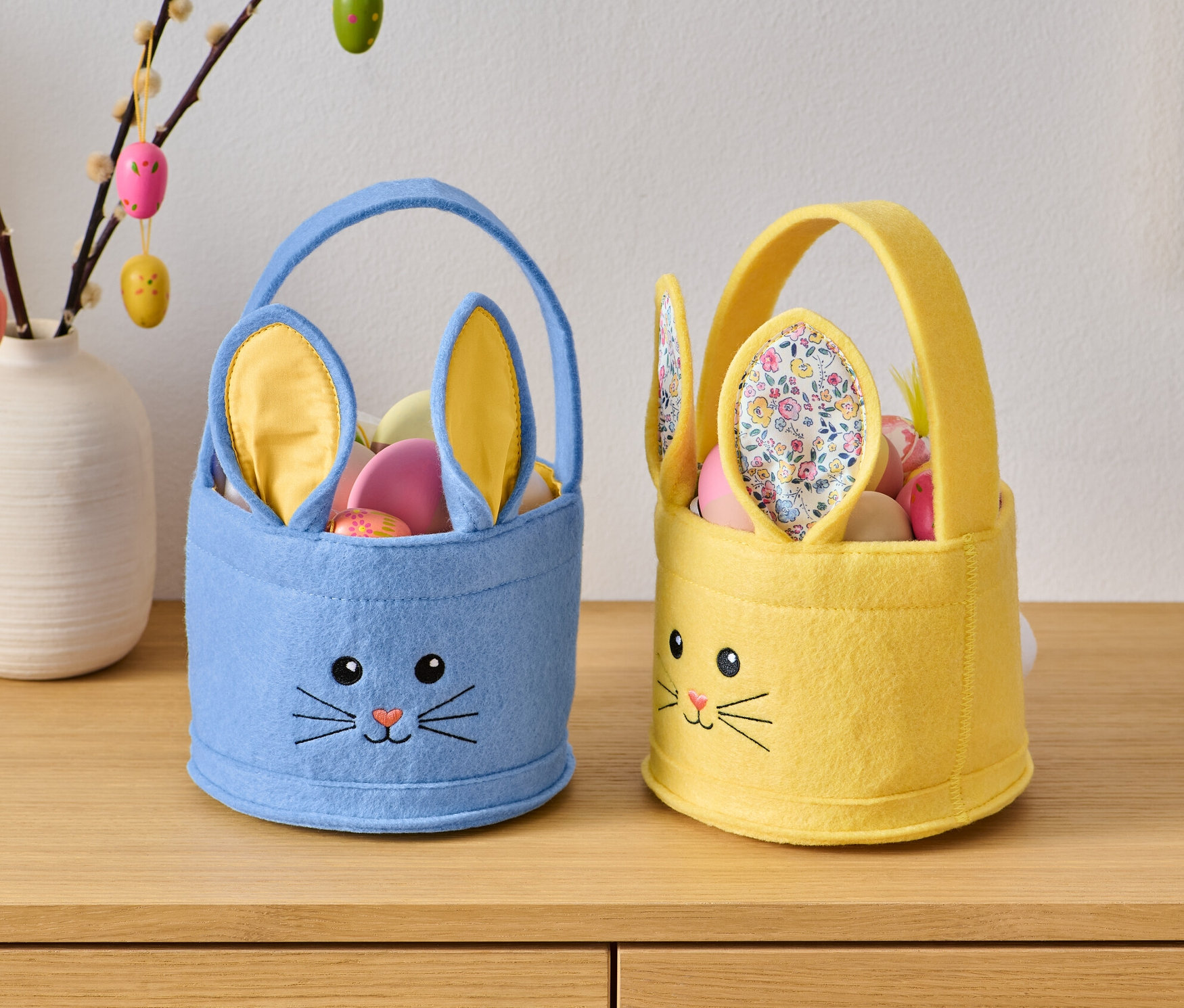Zwei Osterkörbchen mit Hasengesicht stehen auf einer Holzkommode.