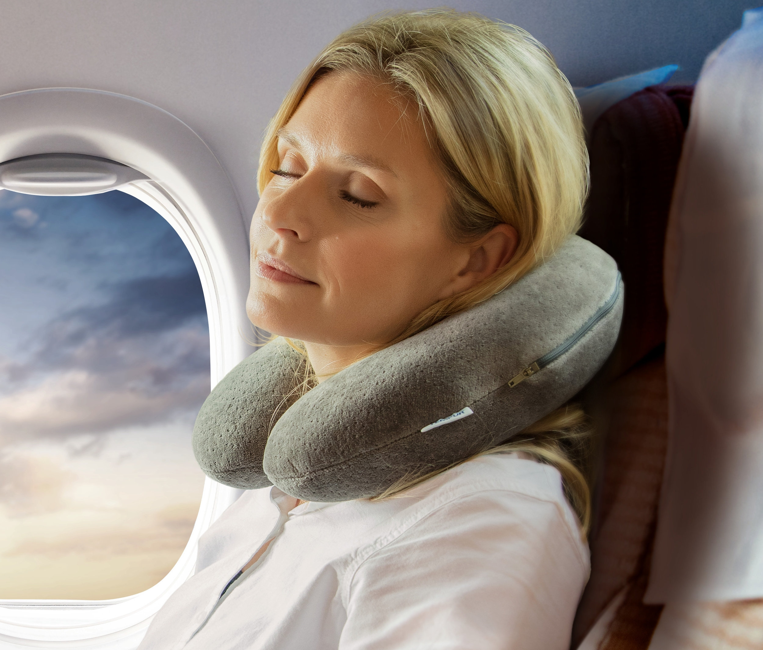 Frau schläft im Flugzeug mit einem grauen TEMPUR® Transitkissen um den Hals.