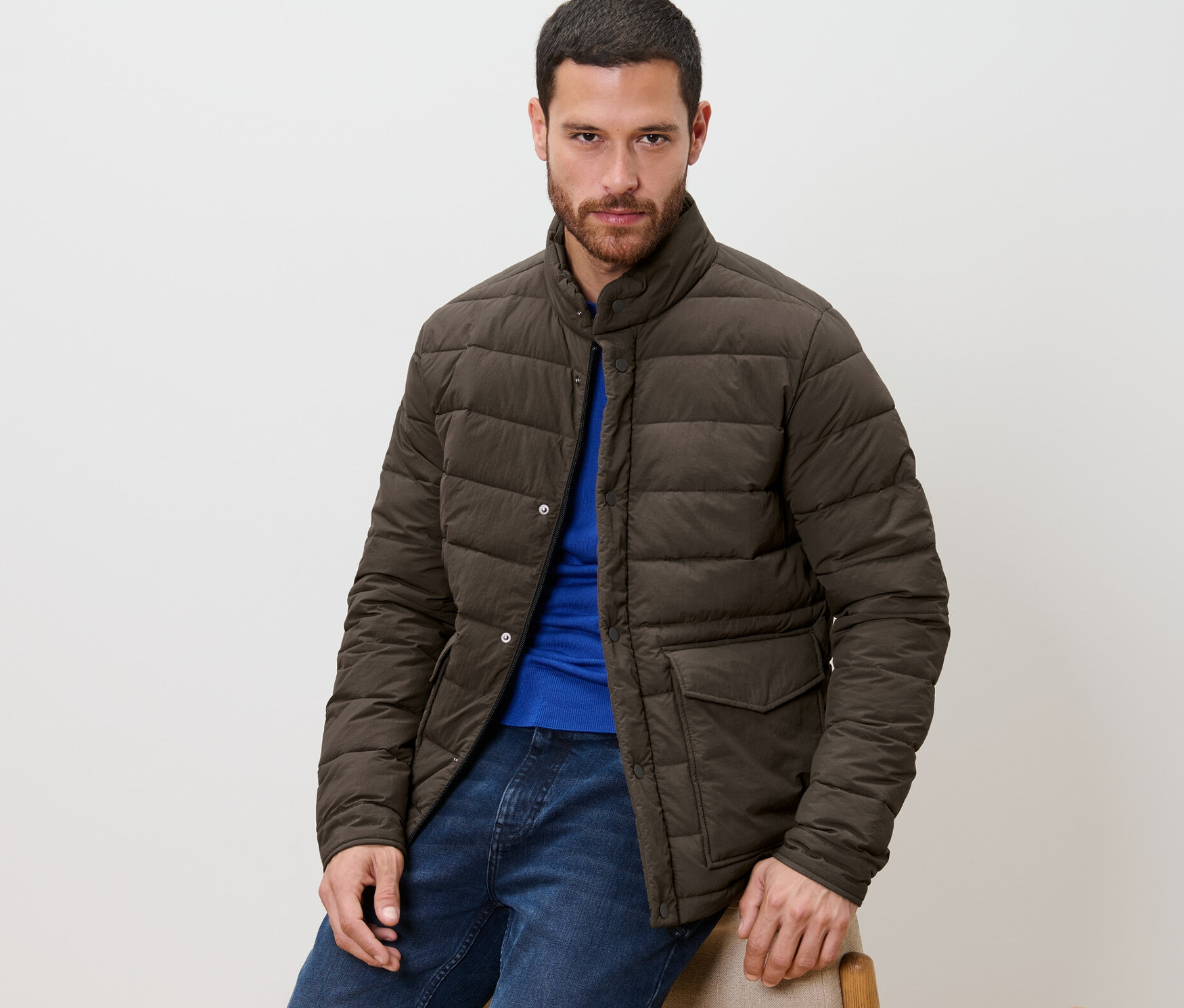 Mann sitzt und trägt eine Steppjacke, blaue Jeans und ein blaues T-Shirt.