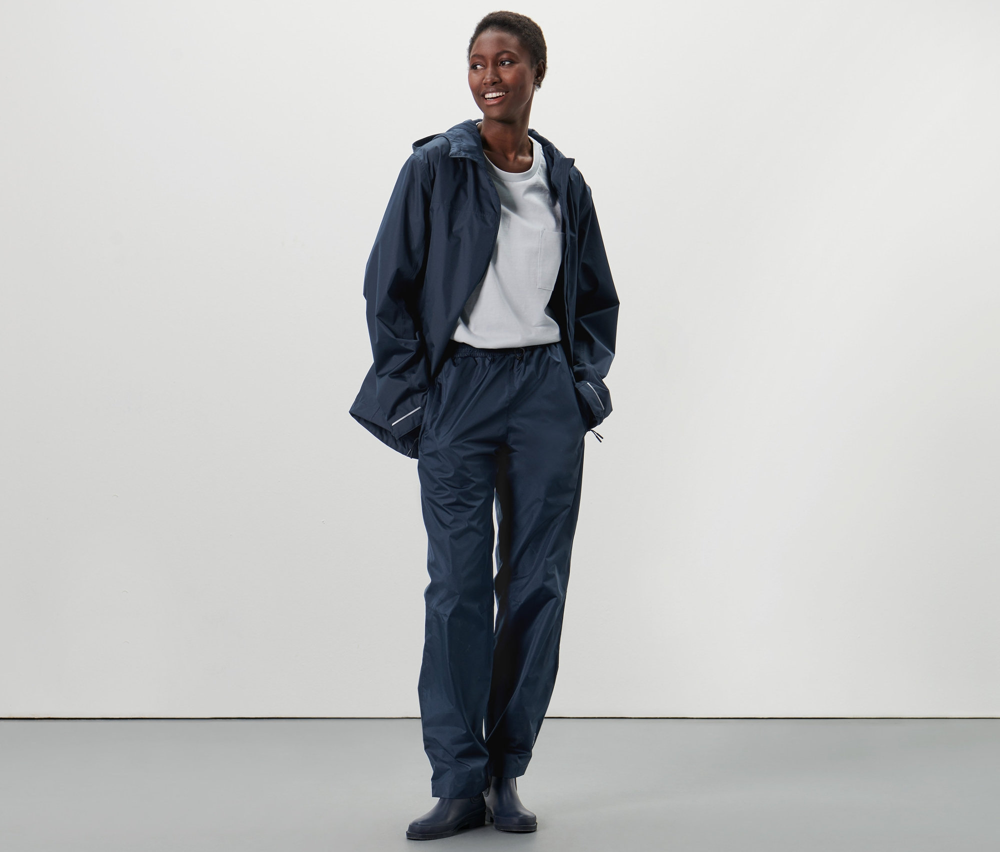 Eine Afroamerikanerin steht und trägt eine Unisex-Regenhose und eine Regenjacke.