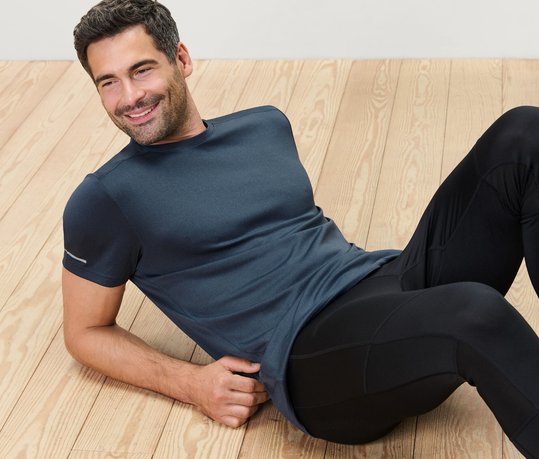 Mann liegt auf Holzboden und trägt ein blau meliertes Funktionsshirt.