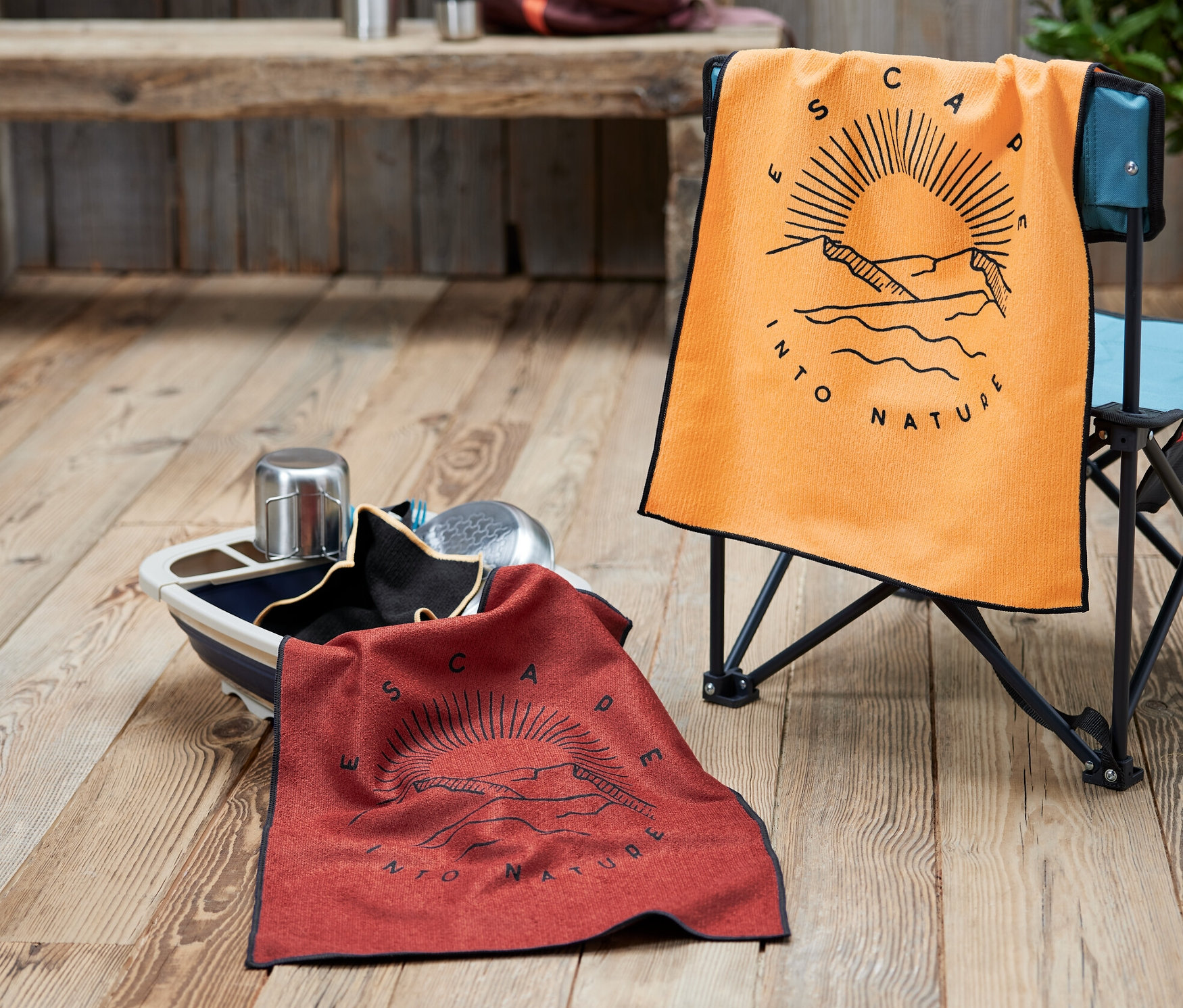 Ein orangefarbenes Geschirrtuch auf einem Stuhl und ein rotes Geschirrtuch in einer Schüssel. Im Hintergrund ein Rucksack und eine Thermoskanne.