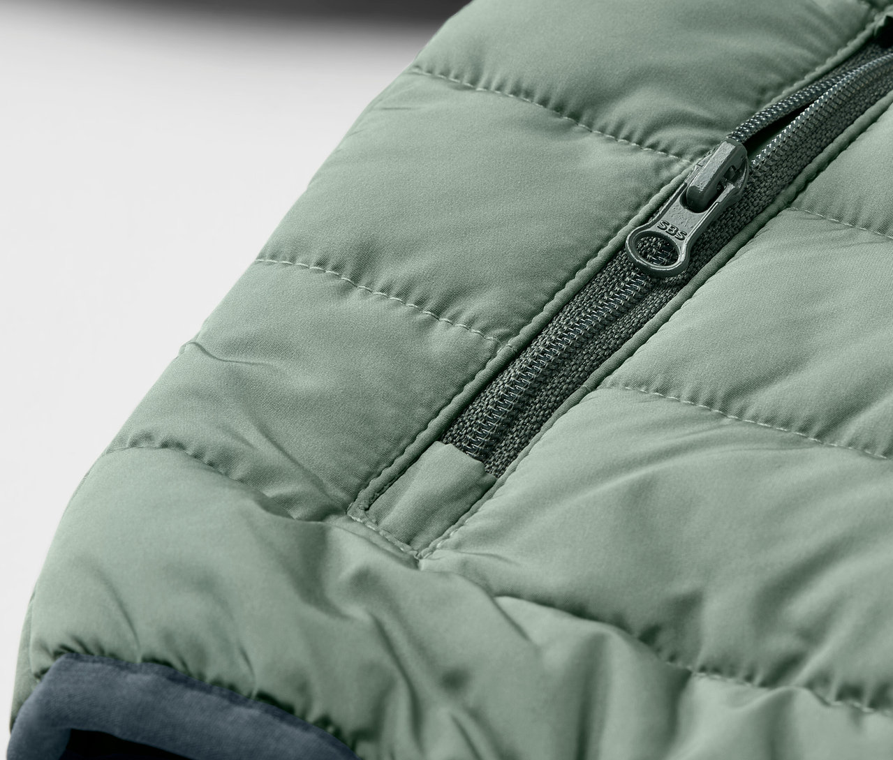 Detail einer grünen Kinder-Steppjacke mit Reißverschluss.