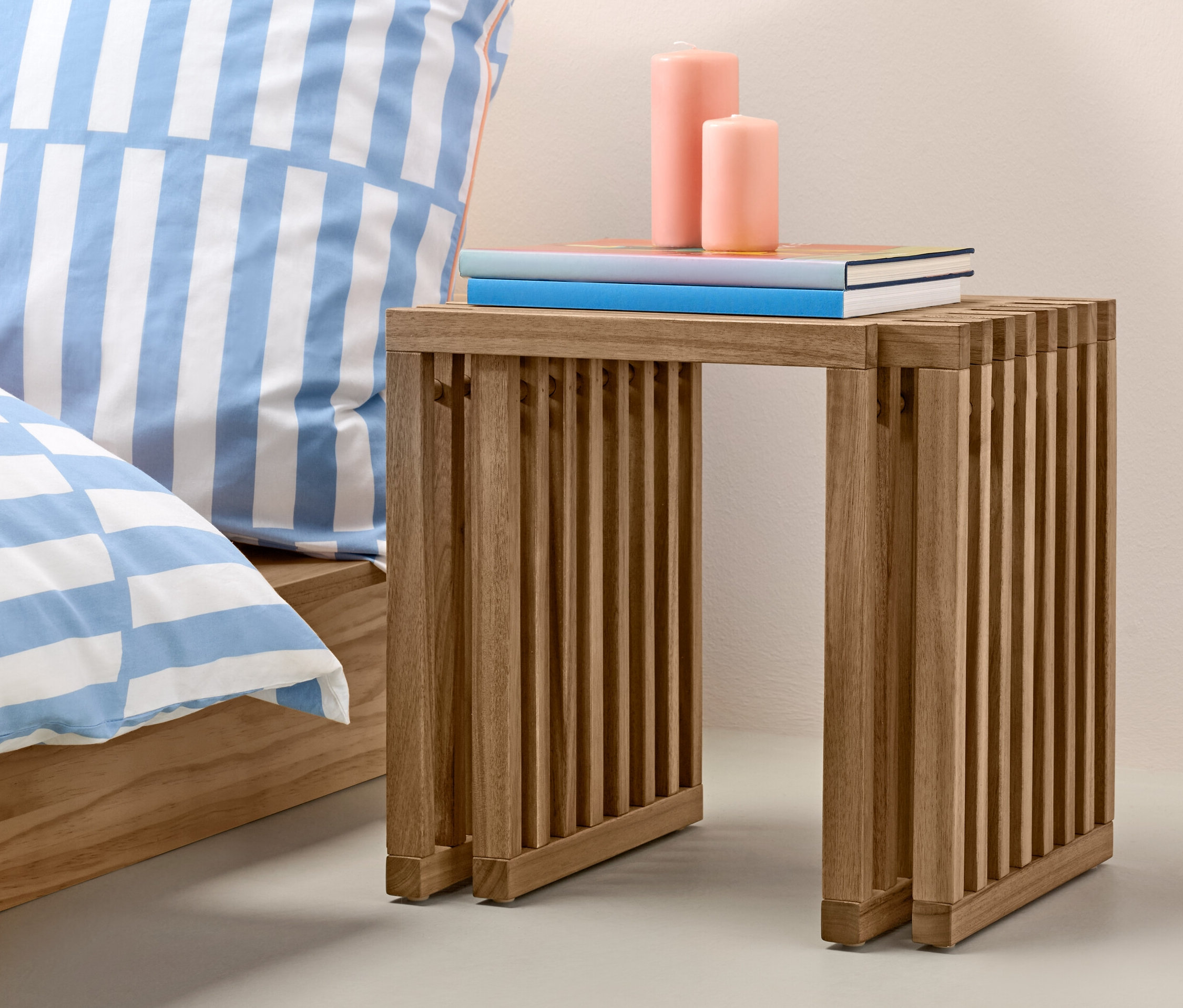 Ausziehhocker mit Büchern und Kerzen neben Bett und orangefarbener Vase.