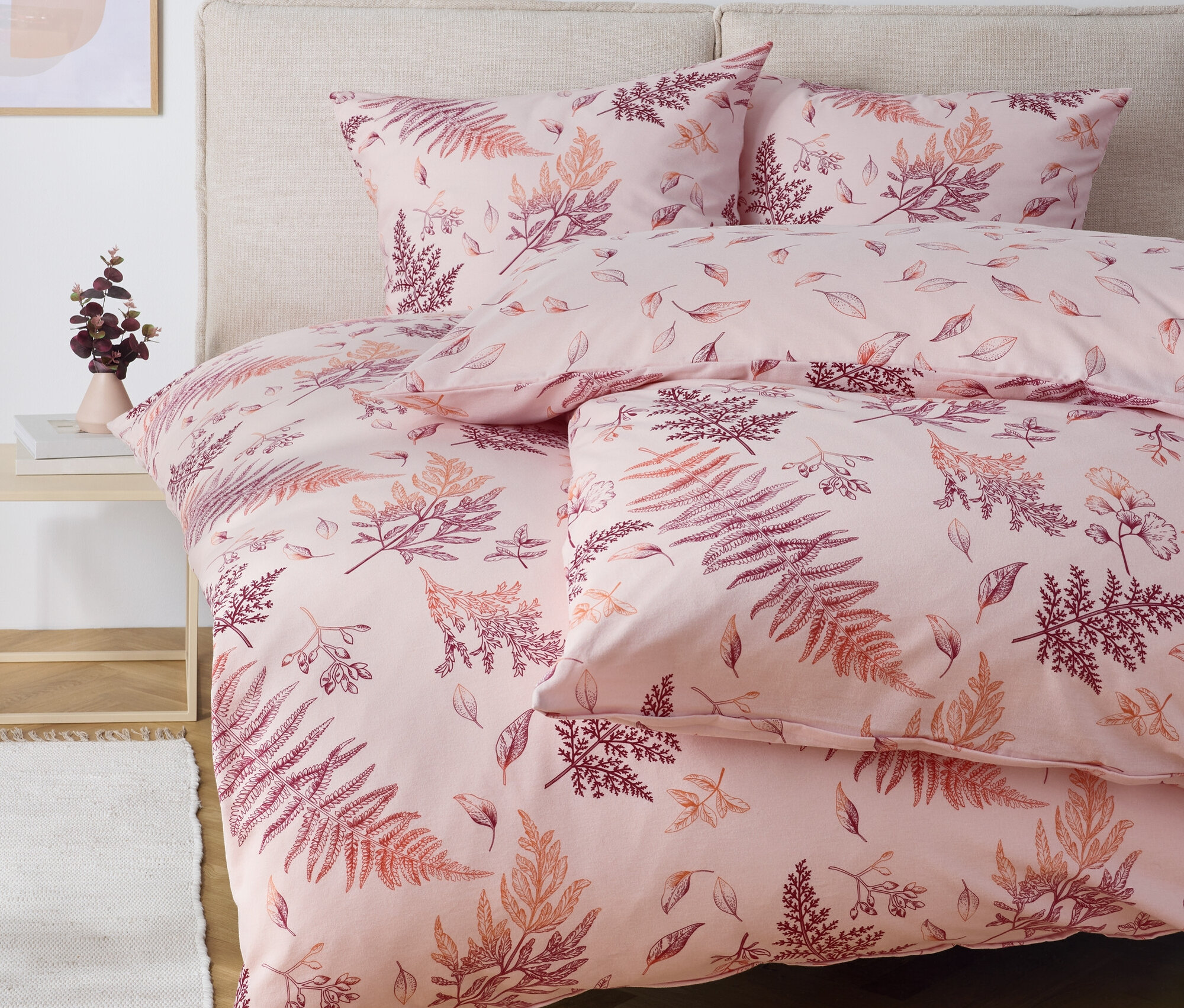 Rosa Bettwäsche mit Farnmuster auf einem Bett.