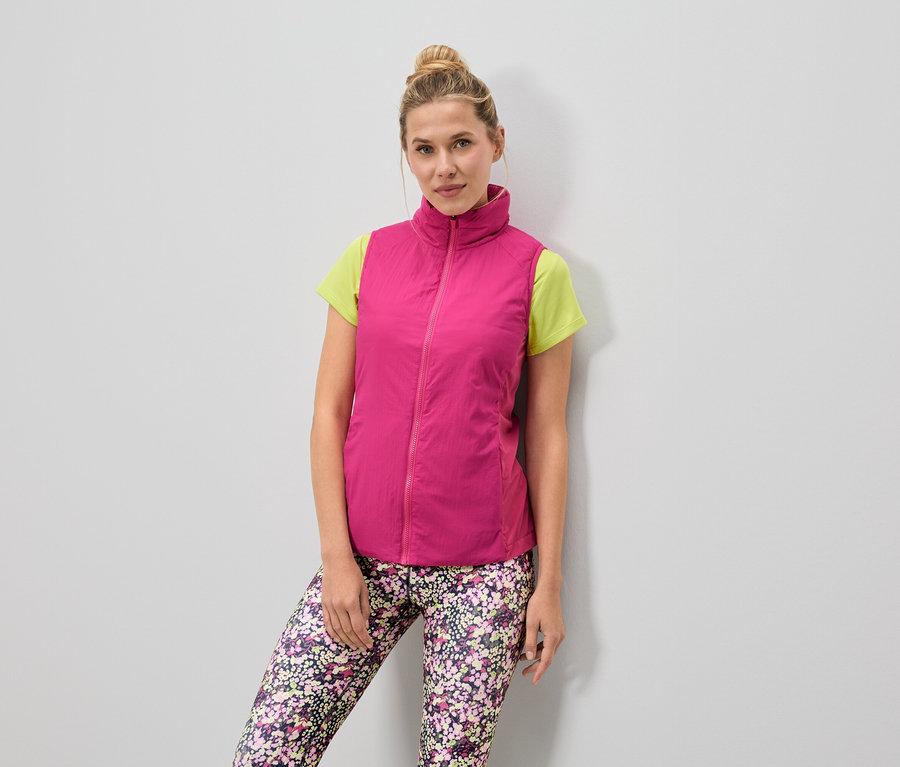 Frau trägt eine pinke Weste über einem hellgrünen T-Shirt und Leggings mit Blumenmuster.