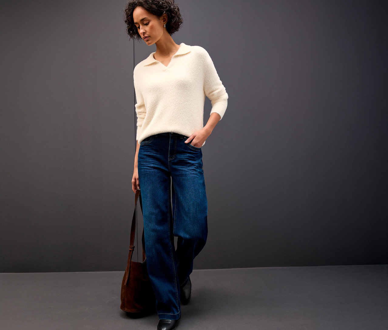 Frau trägt einen Street One Strickpullover mit Polokragen, Bluejeans und eine braune Handtasche.