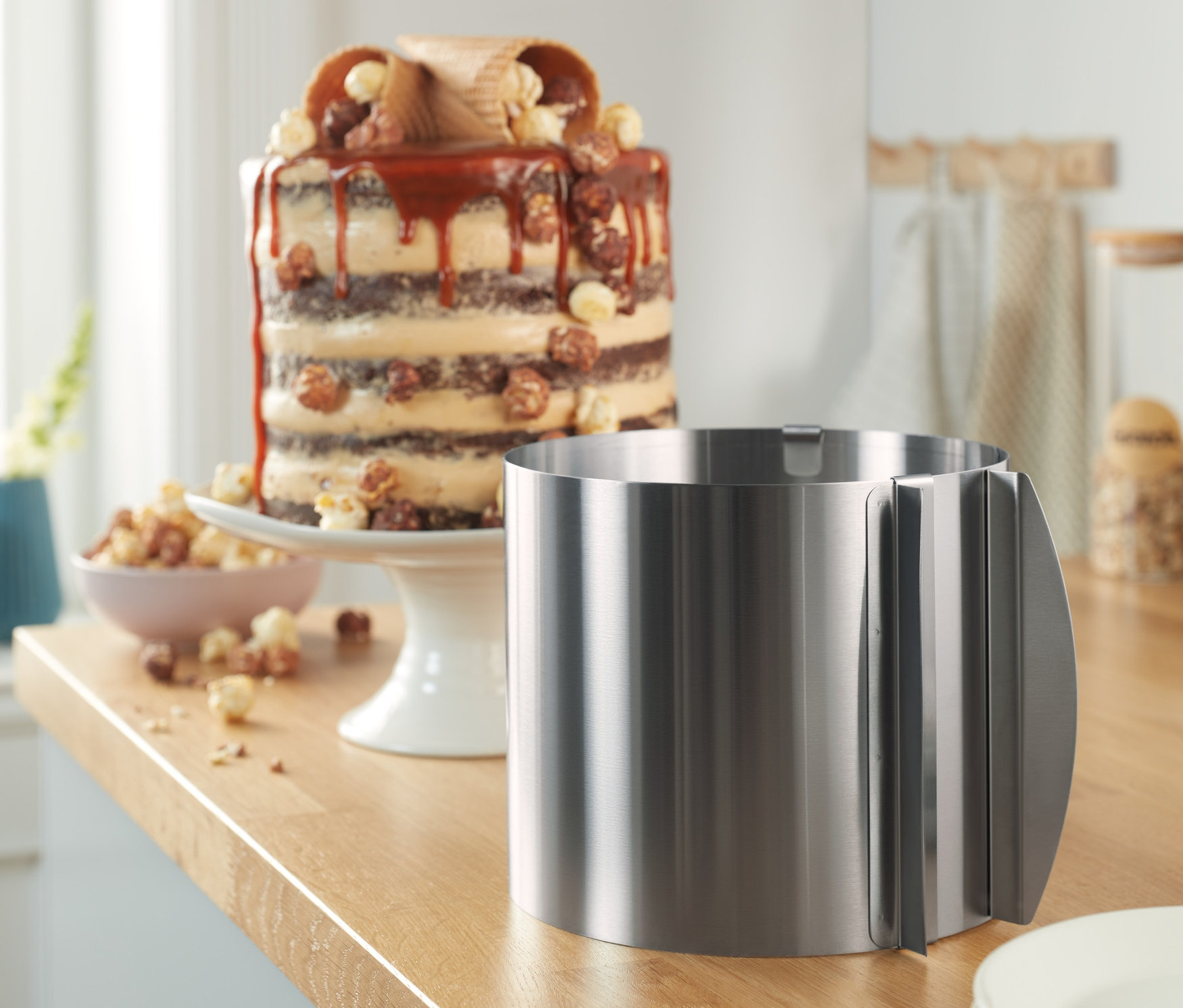 Ein extrahoher Edelstahl-Tortenring steht auf einer Küchentheke neben Tellern und einem Kuchen.