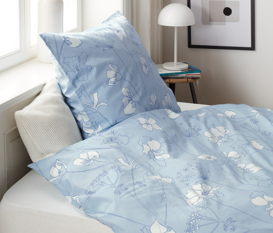 Hellblaue Perkal-Bettwäsche mit Blumenmuster auf einem Bett.