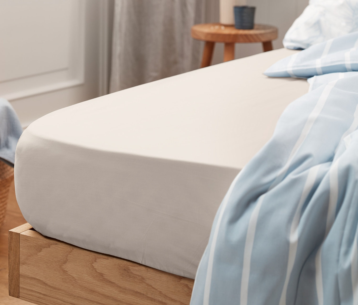 Beiges Jersey-Spannbettlaken auf einem Bett mit Holzrahmen und blau-weiß gestreifter Decke.