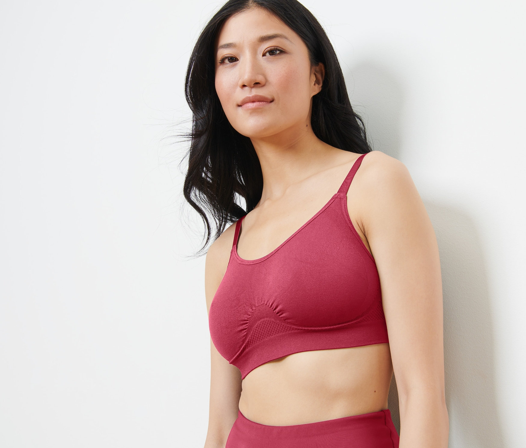 Asiatische Frau trägt einen nahtlosen Sport-BH in Beere-Farbe und schaut nach rechts.