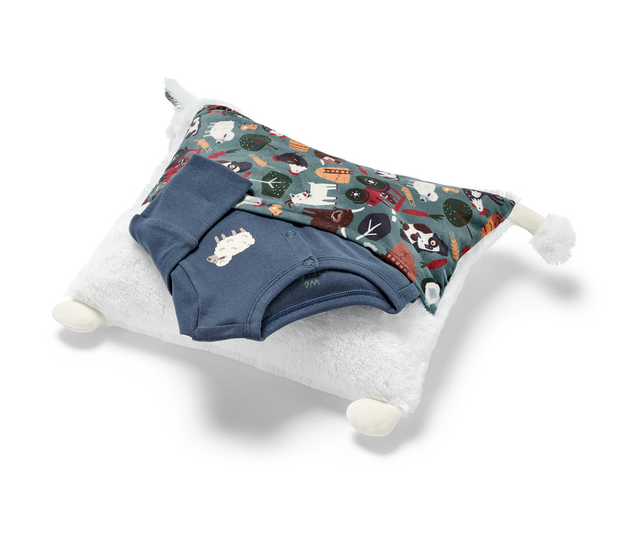 Ein Kuschelkissen »Schaf« mit Pyjamafach, ein Babybody und eine Decke liegen übereinander.