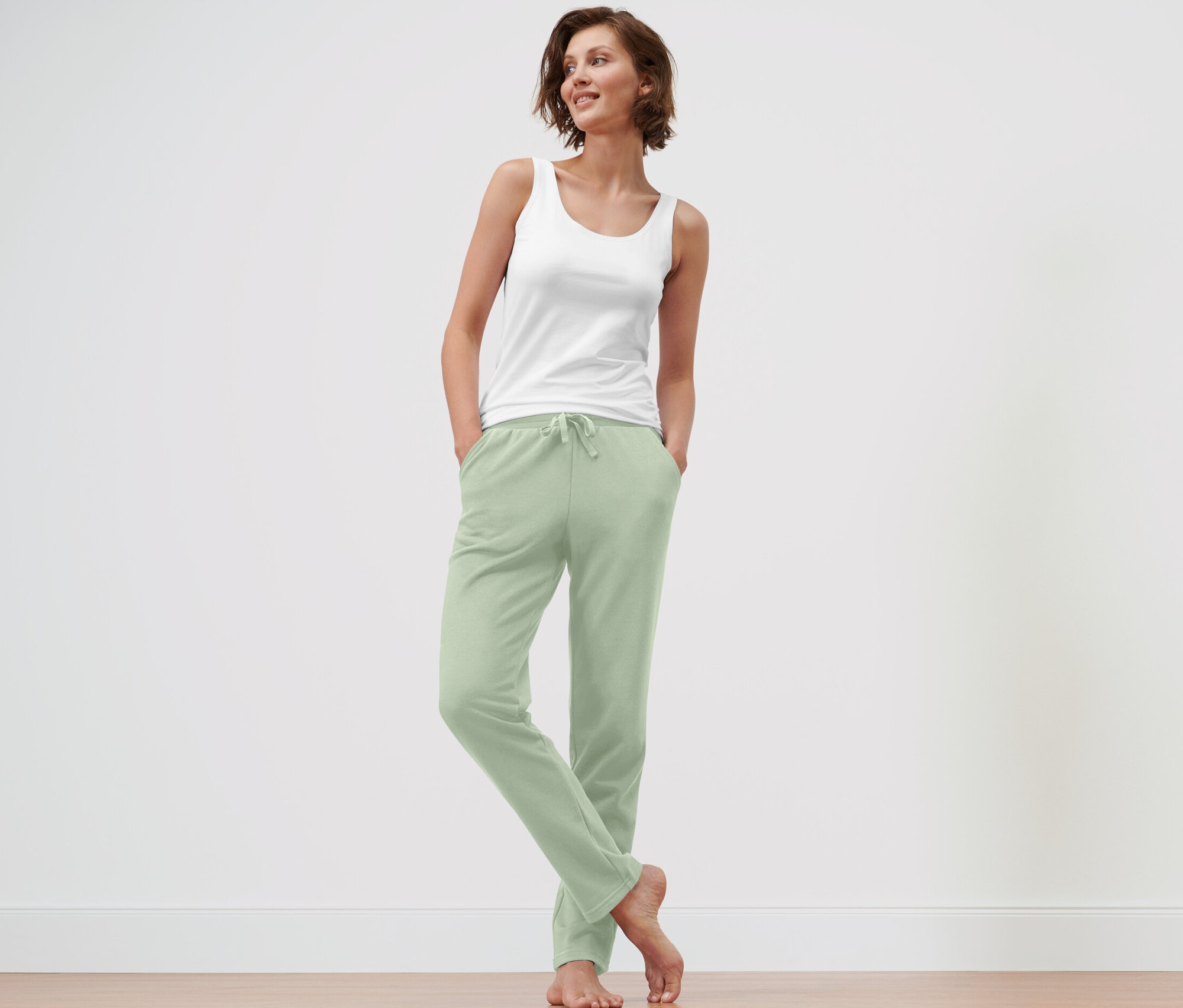 Frau steht mit Händen in den Taschen einer hellgrünen Loungewear-Hose.